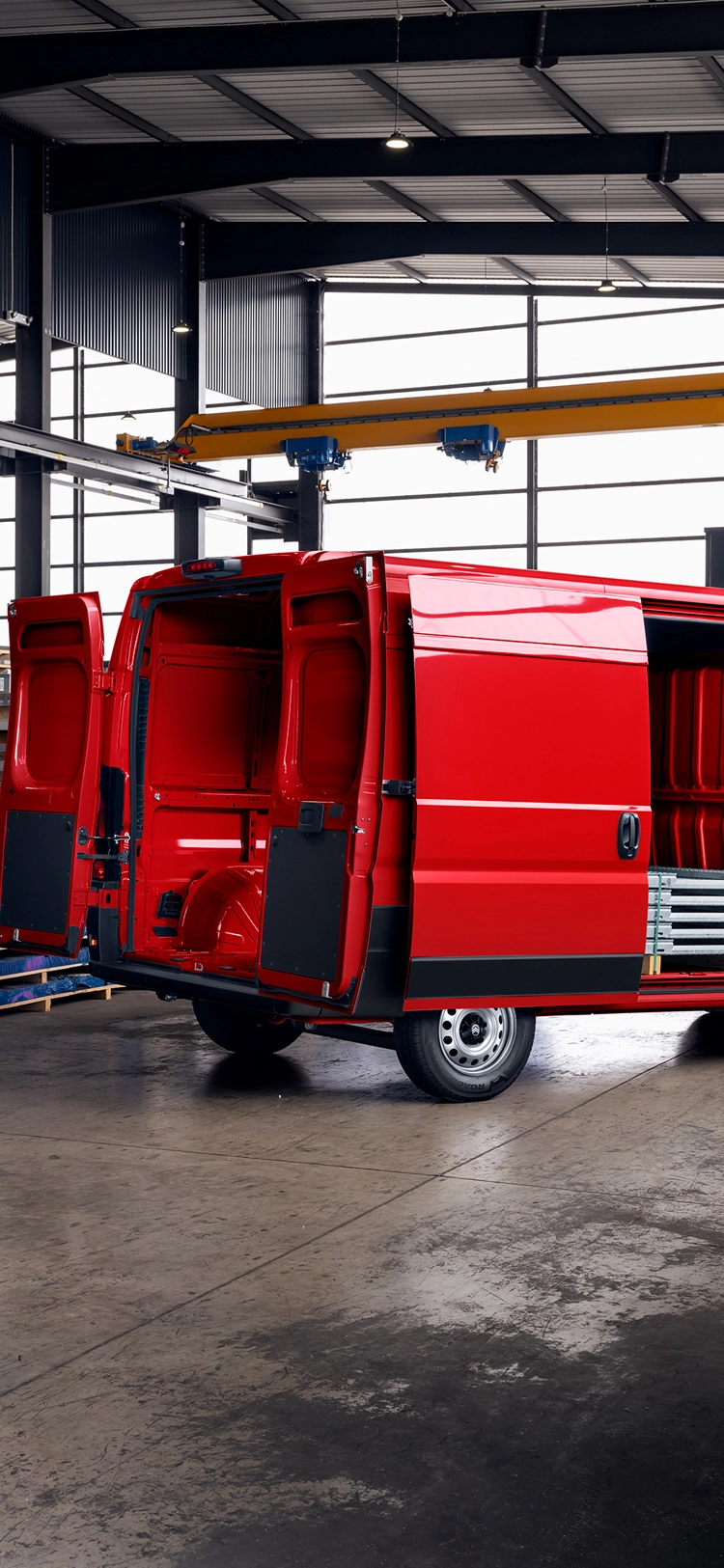 Vista traseira de três quartos de uma Citroën Jumper vermelha com as portas de carga abertas no interior de um armazém, destacando o amplo espaço de carga, a durabilidade e a versatilidade empresarial.
