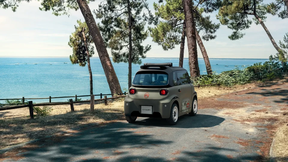 Vista traseira de três quartos do Citroën ami Outdoor junto à costa, apresentando um automóvel urbano elétrico com teto aberto para mobilidade de lazer