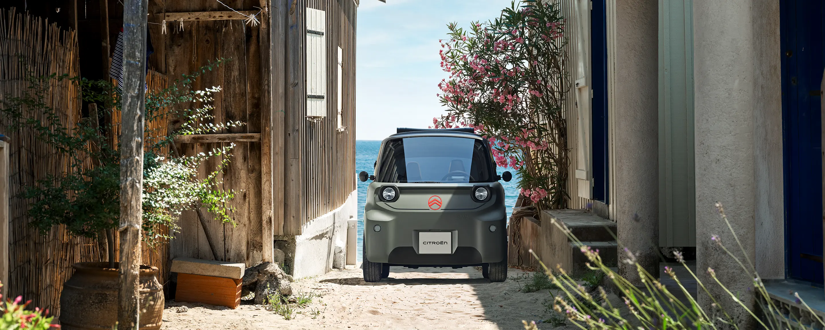 Vista frontal: o Citroën ami Outdoor, com faróis LED, apresenta um automóvel urbano elétrico compacto a circular numa estrada costeira estreita