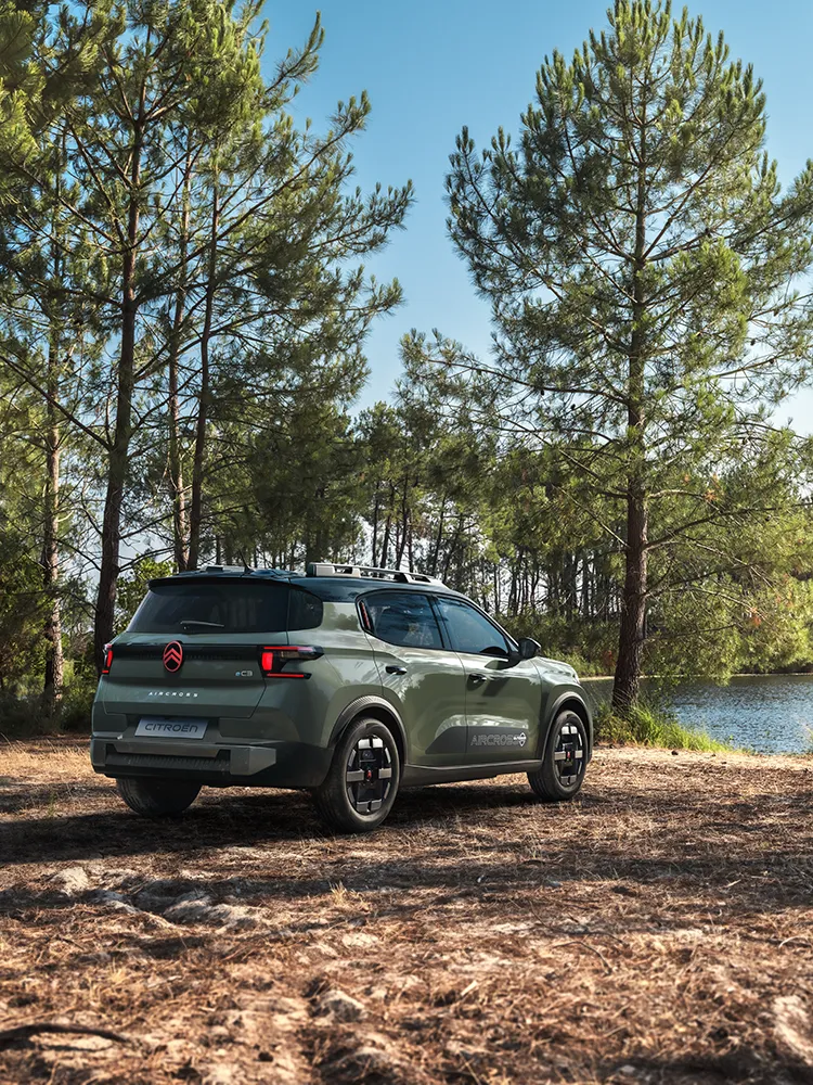 A vista traseira de três quartos do SUV Citroën ë-C3 Aircross mostra a assinatura LED, o Advanced Comfort e o estilo de um SUV familiar numa estrada florestal