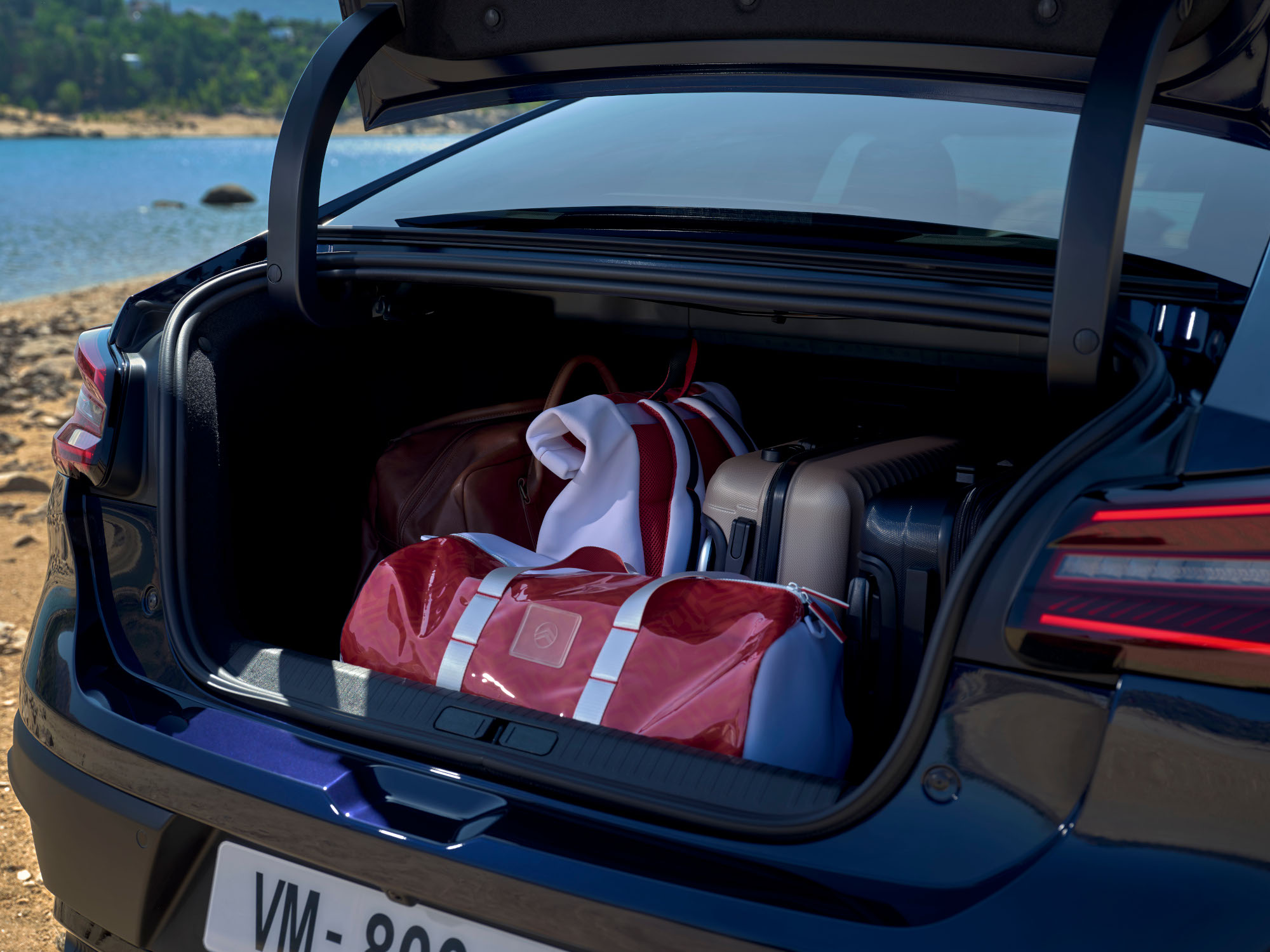 Bagageira aberta do Citroën C4 X carregada com malas de viagem junto a uma localização à beira de um lago.