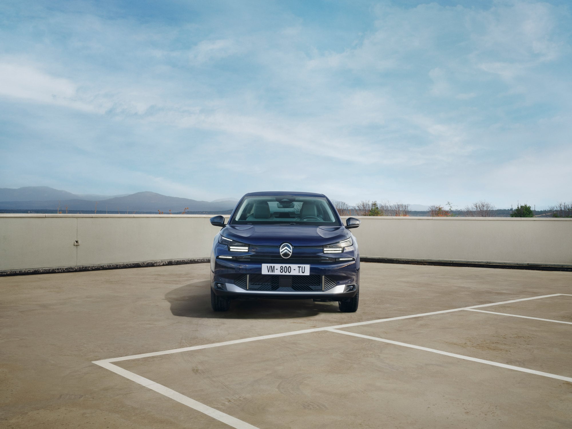 Vista frontal do Citroën C4 X num parque de estacionamento elevado, destacando a sua presença fastback arrojada para uma mobilidade confiante e acessível.