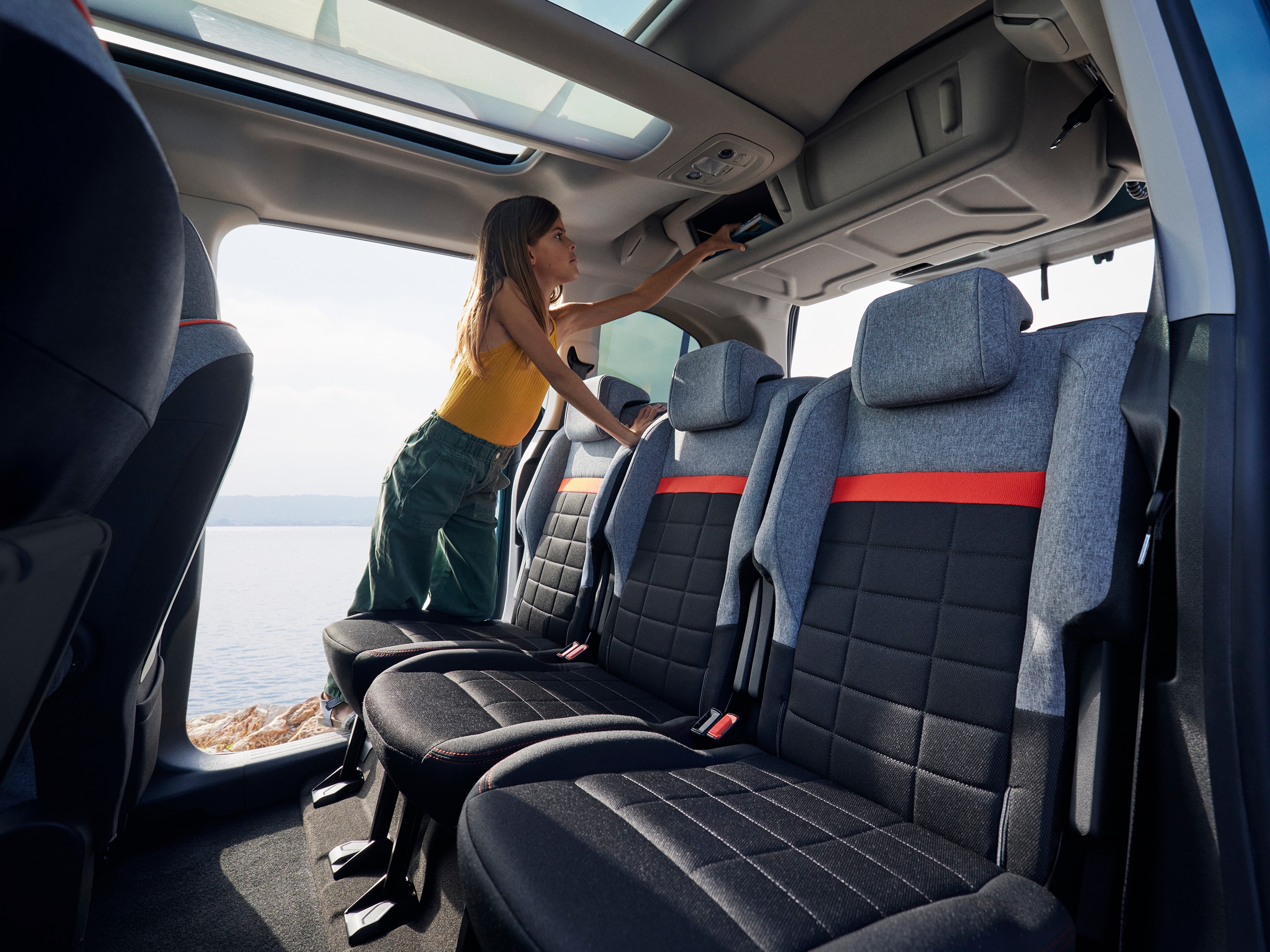 Vista interior traseira do ë‑Berlingo, destacando os compartimentos de arrumação superiores para maior praticidade e conveniência familiar.