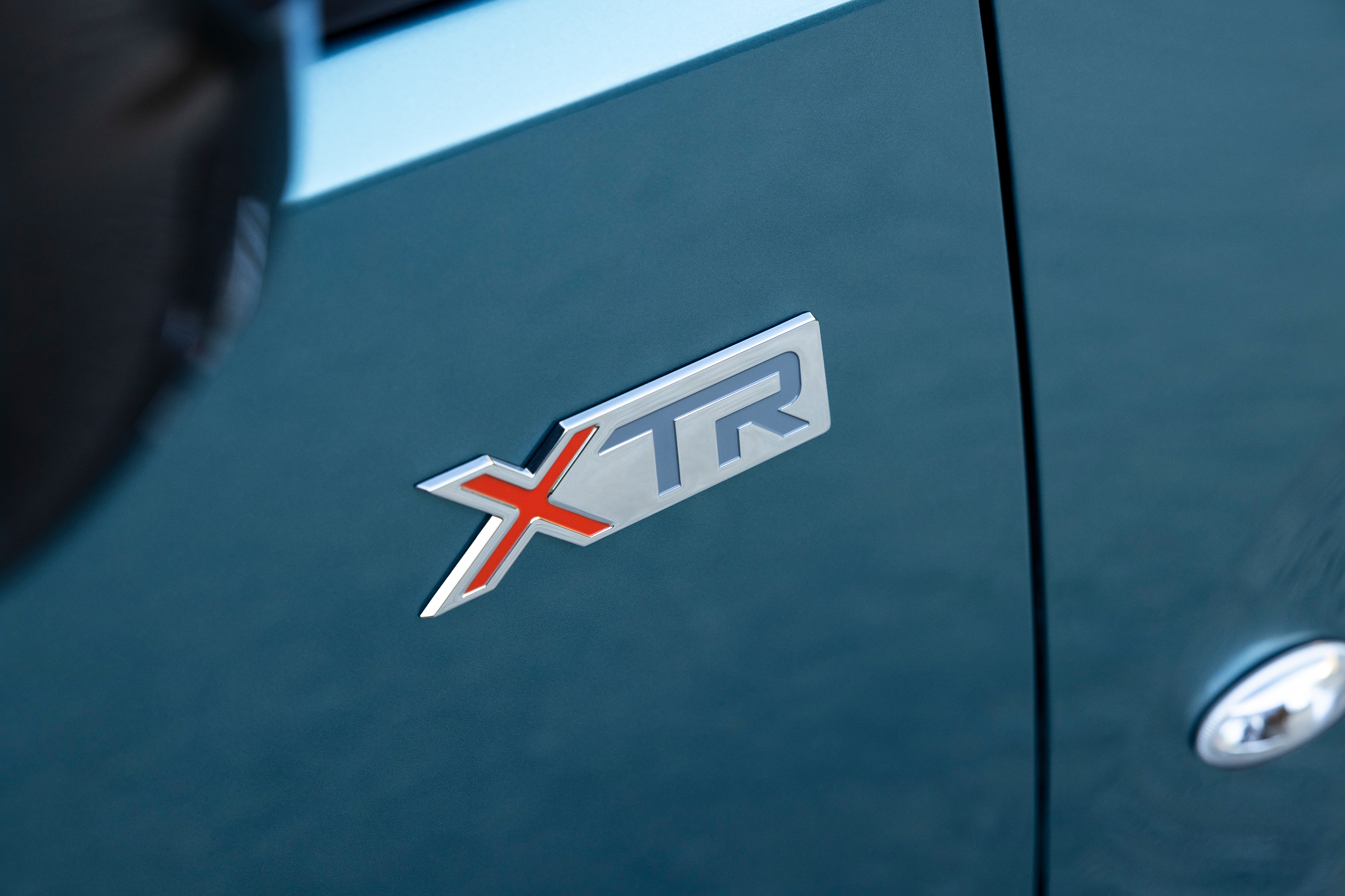 Grande plano do emblema XTR do ë‑Berlingo, destacando o seu design distintivo, qualidade e robustez, reforçando a identidade exclusiva da versão.