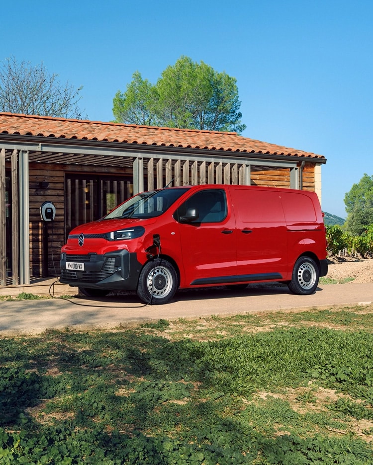 Vista lateral de três quartos do exterior de um Citroën ë-Jumpy vermelho a carregar em frente a um edifício, mostrando o design elétrico moderno, a praticabilidade no dia a dia, a conectividade e a presença profissional e confiante.