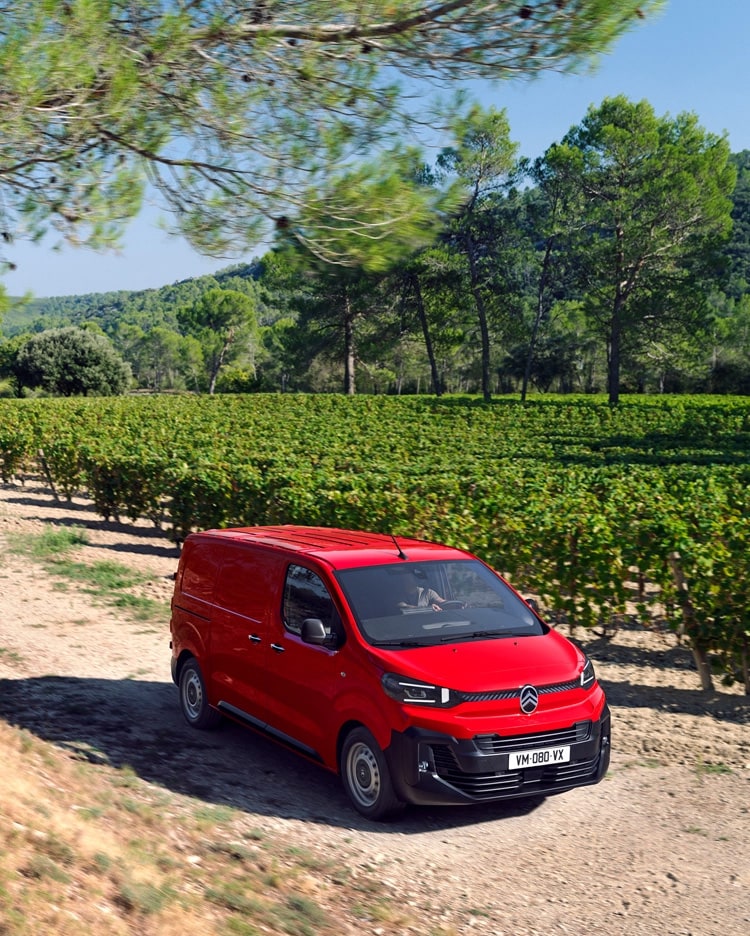 Vista frontal de três quartos de um Citroën Jumpy vermelho a circular numa estrada rural, mostrando um design robusto, conforto de condução, versatilidade e presença segura.