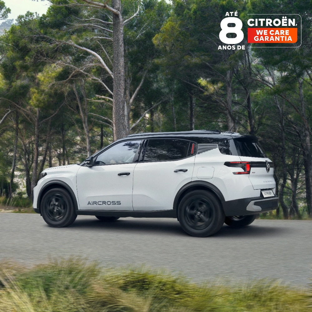 Vista traseira de três quartos do Citroën ë-C3 Aircross, com o SUV elétric , a circular numa estrada florestal destacando o design premiado e a cobertura de 8 anos para uma mobilidade acessível.